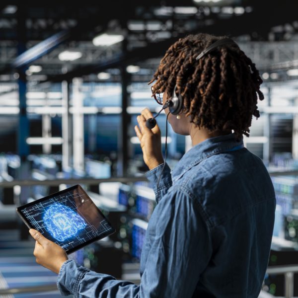 Server hub IT specialist monitoring systems and doing tech support, guiding users through troubleshooting steps. African american expert providing remote diagnostics using headset mic.