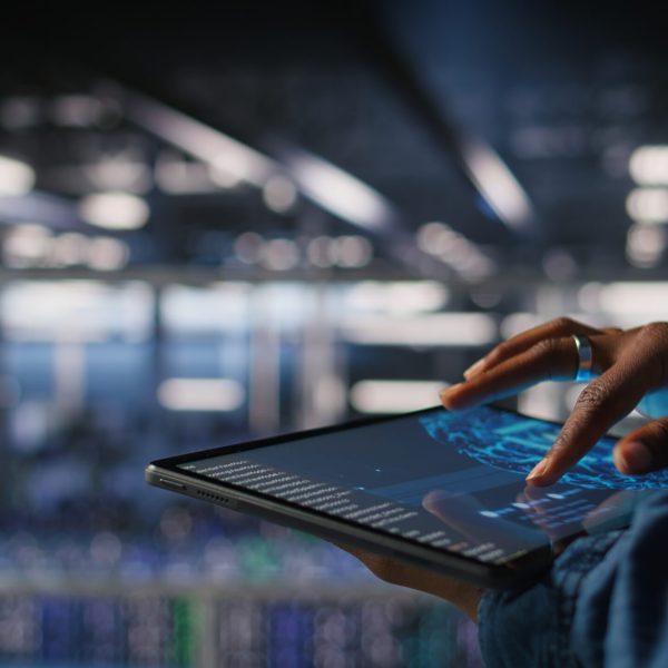 Close up of data center engineer using tablet, doing maintenance on rigs handling AI processing tasks. Server hub computer scientist managing storage arrays supporting deep learning tech,